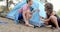 Two women are setting up a blue tent in a wooded area