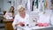 Two women sitting at the tables working on clothing manufacture. Woman sewing pink cloth on modern machine and cutting