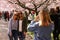 Two women with sunglasses have taken their photo under a blooming japanese cherry blossom tree.