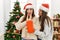 Two women surprise with gift standing by christmas tree at home