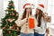 Two women surprise with gift standing by christmas tree at home