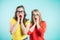 Two women surprise holds cheeks by hand. Beautiful girls on a blue background. Expressive facial expressions