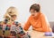 Two women talking each other. Woman wearing glasses, orange sweater listening other woman in front of her in office