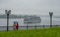 Two women under an umbrella in rainy weather standing on the embankment of the river and escorted the ships that are hiding in the