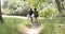 Two women walk along a narrow trail in a lush, green forest setting, collecting trash