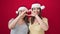 Two women wearing christmas hat doing heart gesture over isolated red background