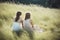 Two women in white dresses sitting in windy summer breeze on grass. Generate ai
