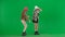 Two women in white and pink balaclavas dancing merrily. Freak women in fur coats on green studio background. Fashion