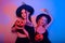 Two women witches hold pumpkins in their hands and dance. Women in neon lights are celebrating a Halloween party. Models smile and