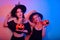 Two women witches hold pumpkins in their hands and dance. Women in neon lights are celebrating a Halloween party. Models smile and