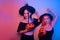 Two women witches hold pumpkins in their hands and dance. Women in neon lights are celebrating a Halloween party. Models smile and