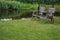 Two wooden chairs in the backyard near pond. Old outdoor furniture in summer garden. Empty quiet place for relax.