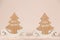 Two wooden ornaments in the shape of fir with soft pink background