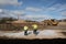 Two workers in high vis jackets and hard hats on a construction site with dumper digger truck