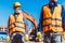 Two workers in reflective vests and hardhats standing