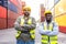 Two workers in safety helmets standing in a busy freight yard.