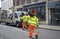 Two workers on their back carrying road traffic cones stacked on each other on their shoulder.