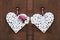 Two woven white hearts with peonies and daisies hanging on a wooden wall.