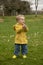 Two year old boy in yellow raincoat and welly boots playing outdoors