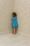 Two-year-old girl in blue dress stands punished in corner