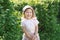 Two year-old laughing girl in corduroy flat cap at green garden shrubbery background