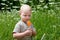 A two-year-old sad and pensive boy eats a lollipop in a summer meadow