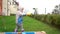 A two-year-old toddler plays with yellow scoop in an outdoor sandbox in a kindergarten. The child is dressed in boots