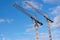 Two yellow construction cranes against blue sky with a few cloud