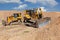 Two yellow dozers on a dirt terrain with blue sky