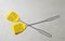 Two yellow fly swatters lying on a gray picnic table