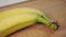 Two yellow ripe bananas in a bunch close-up on a wooden cutting board with peel and green stem.