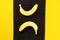 Two yellow ripe bananas from the tropics on a black bamboo napkin on a yellow fabric background with space for text