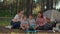 Two young 30s mothers and two boys cooking on frying pan sitting on picnic blanket on summer camping vacation with tent