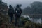 Two young adult hiker walking near small lake surrounded by paramo vegetation with bushes and trees in the rain forest on Ena hill