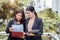 Two young Asian businesswomen looking into document file folder for analyzing profit or sale break even point after marketing.