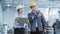 Two Young Asian Heavy Industry Engineers in Hard Hats Walking with Laptop Computer and Talking in a