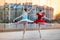 Two young ballerinas in a bright red and blue tutu are dancing against backdrop of the reflection of city sunset