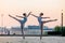 Two young ballerinas dancing in pointe shoes in city against the backdrop of sunset sky