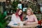 Two young beautiful girls sit in a green cafe at a table. Drink tea with croissants, chatting, laughing and taking