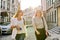 Two young beautiful happy women university students walking along city street