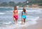 Two young beautiful tanned women walking along sandy beach