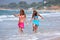 Two young beautiful tanned women walking along sandy beach