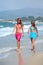 Two young beautiful tanned women walking along sandy beach