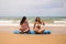 Two young and beautiful women sitting on a surfboard on the shore of the beach. The women are enjoying their trip to the beach
