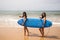 Two young and beautiful women with a surfboard on the shore of the beach. The women are enjoying their trip to the beach paradise