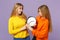 Two young blonde twins sisters girls in vivid colorful clothes holding round clock, moving arrows isolated on pastel