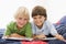 Two Young Boys Lying Down On A Bed Reading A Book