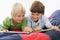 Two Young Boys Lying Down On A Bed Reading A Book