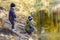 Two young boys playing fishing with sticks near pond in fall park. Little brothers having fun near lake or river in autumn. Happy