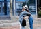 Two young brunette girls, wearing casual jeans attire, hugging in front of blue modern glass building. Girlfriends meeting in city